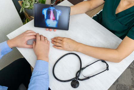 Shot of the female doctor in uniform showing x-ray image of the lungs on the tablet to the patient