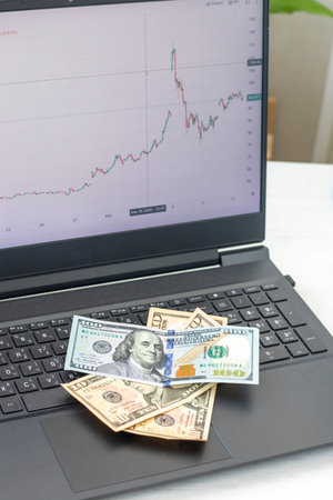 A candlestick chart for a crude oil, on a laptop screen, showing some pretty significant volatility after events in middle east in march 2026. Notes amounting 120 dollars on the laptop keyboardの写真素材