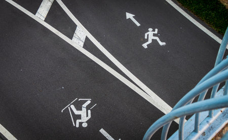 Top view of an asphalt sports path showing white painted road markings for roller skating and Nordic walking lanes.