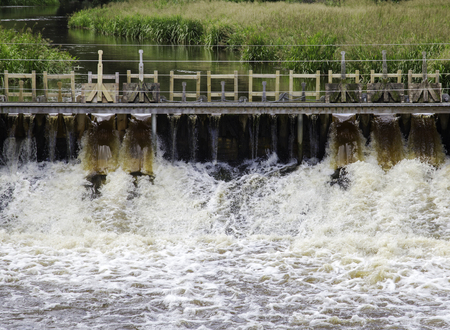 Foamy water flowing through sluice beneath narrow wooden bridgeの写真素材