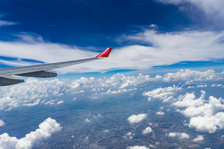 View from airplane window showing airplane wing with blue sky and white cloudsの写真素材
