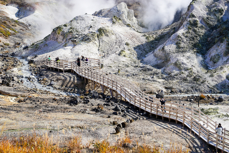 Noboribetsu, Japan - October 25, 2017 : Unknown tourists waling on wooden path at Noboribetsu Jigokudani or Hell Valley in Hokkaido, Japan. Autumn season, red leaves, blue sky and sulfur gas steaming out from ground.のeditorial素材