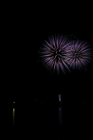 Colorful fireworks of various colors over night sky with reflection on water