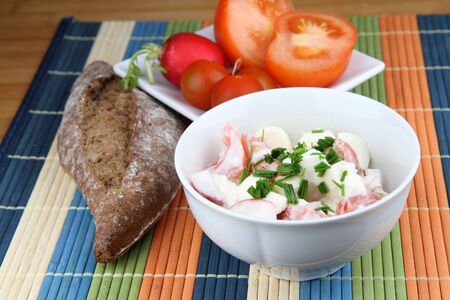 Salad from mozzarella, yogurt, tomato and radish in bowl. Vegetable on white plate and whole bread.の写真素材