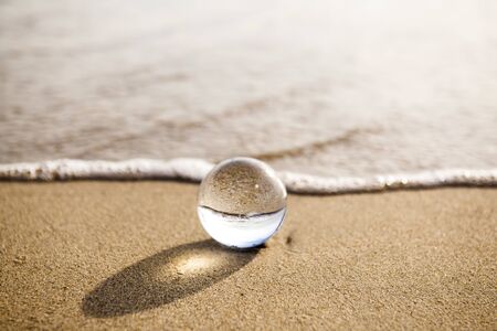 glass ball crystal clear reflecting the sea and beach in the morningの写真素材
