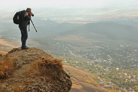 man on the edge of a cliff photographing the landscape of the valleyの写真素材