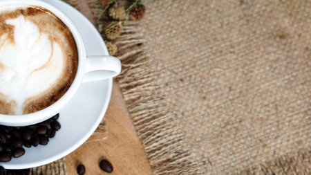 Cappuccino or latte coffee. A cup of latte, cappuccino or espresso coffee with milk put on a wood table with dark roasting coffee beans. Drawing the foam milk on top.の写真素材