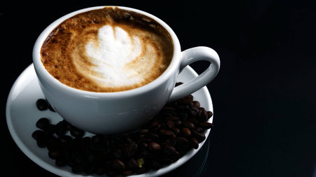 Hot cappuccino with streamed milk. Pour the hot latte art by milk. A cup of strong espresso coffee put on the black glass background with shiny dark roasted Italian coffee beans. Aroma and flavor coffee beverage.の写真素材