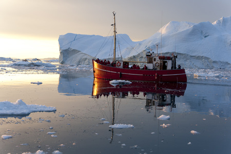 Red fishing boat floating around icebergs at Disko Bay, Ilulissat, Greenland
