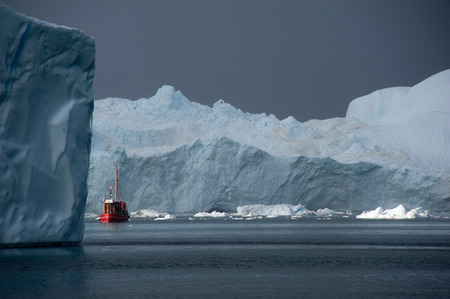 Red fishing boat floating around icebergs at Disko Bay, Ilulissat, Greenlandの写真素材