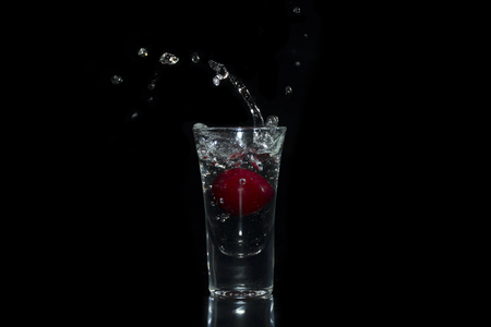 Water splash, cherry in glass on black backgroundの写真素材