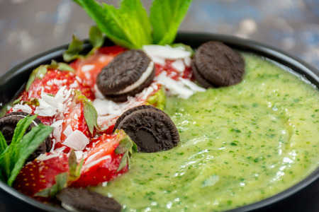 Green smoothie bowl with strawberries, coconut flakes and chocolate cookiesの写真素材