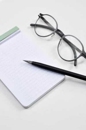 Eye glasses, blank notepad, and mechanical pencil on the tableの写真素材