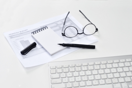 Balance sheet, eye glasses, blank notepad, and pen on the tableの写真素材