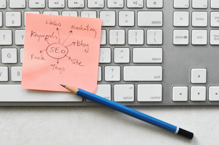 Sticky note with seo plan on computer keyboard and pencil on table