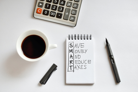 Coffee cup, spiral notebook, calculator, and pen on white background, with handwritten Save Money And Reduce Taxes- taken in natural light with strong shadow to create realistic indoor moodの写真素材