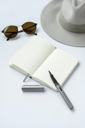 Sunglasses, notebook, pen, and hat, on white background - taken in natural light with strong shodow to create realistic indoor moodの写真素材
