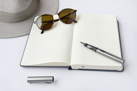 Sunglasses, notebook, pen, and hat, on white background - taken in natural light with strong shodow to create realistic indoor moodの写真素材