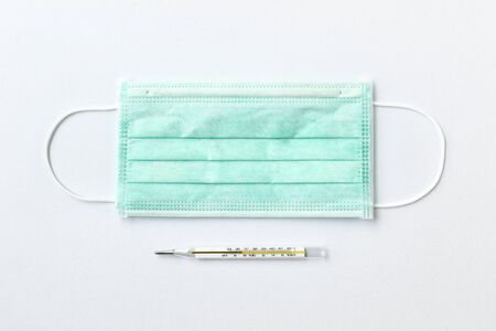 Still life of a green face mask and a mercury thermometer on white backgroundの写真素材