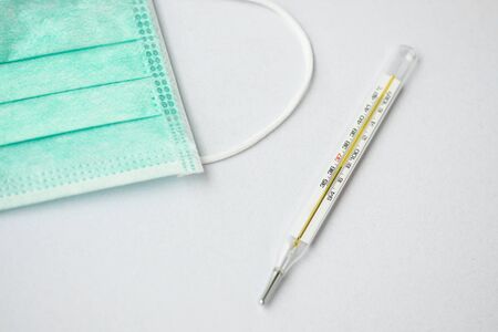 close-up shot of a mercury thermometer and a green face mask on white backgroundの写真素材