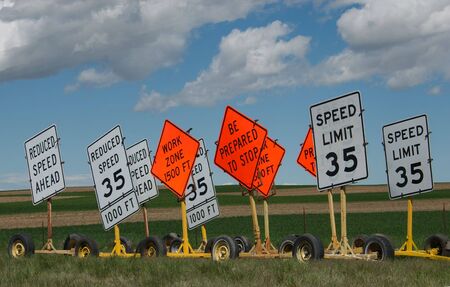 Construction zone signs against a blue cloud filled sky setting near some farmland