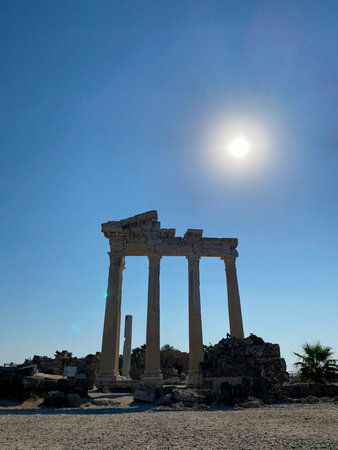 The sun shines brightly over the weathered stone columns and rubble of an ancient archaeological site, hinting at past grandeurの写真素材