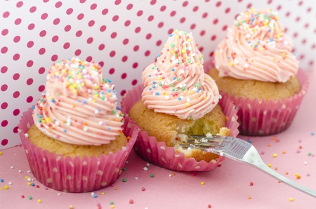 Delicious birthday cupcake with twirled pink icing decorated with colourful sprinkles and a candle...