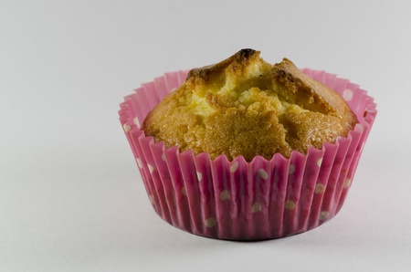 Closeup of a delicious freshly baked golden cupcake or muffin in a pink dotted cup on a neutral...