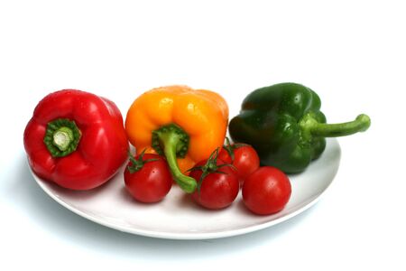 some red, green and yellow peppers on a plate with red tomatoesの写真素材