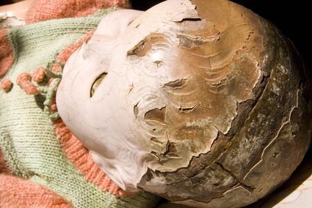 Old antique childs doll with creepy face, cracked and worn, has seen better days.の写真素材
