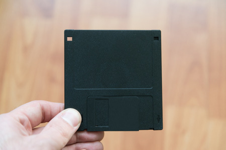 Man holding 3,5 blank new diskette with wooden background