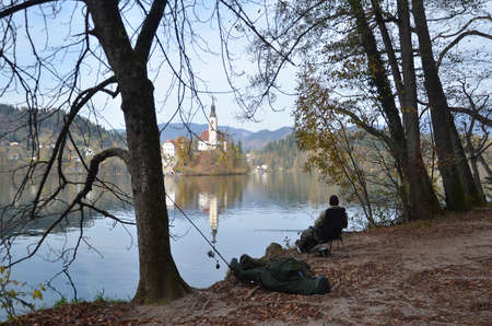 Silhouette of a man fishing at Lake Bled, and facing to the Assumption of Mary Pilgrimage Church during autumn time.のeditorial素材