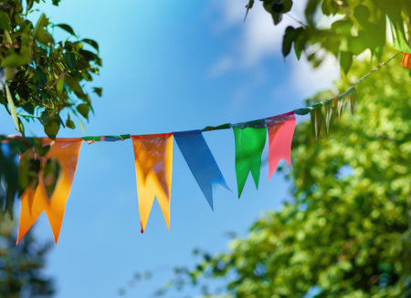 colorful pennant string decoration in green tree foliage on blue sky, summer party background.の素材