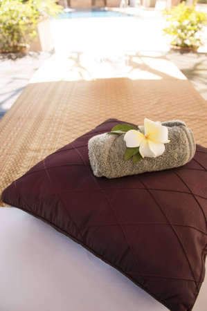 A bed near swimming pool with pillow and towelの写真素材