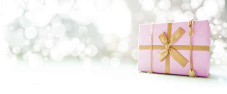 Pink Gift box with gold ribbon and gold decorations. Bokeh background. Side view. Copy space.の写真素材
