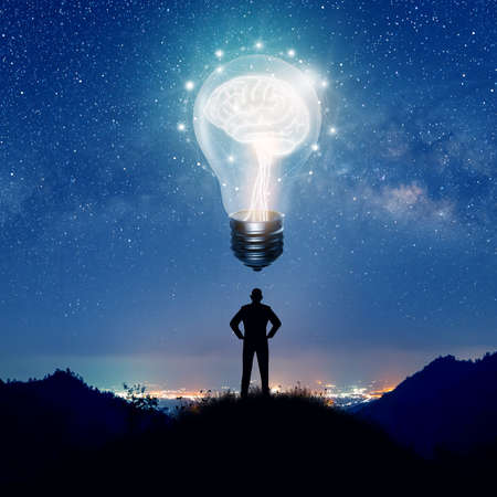 Silhouette of Businessman on hill thinking idea. Light bulb with brain inside and low poly wireframe outside over City and Milky Way background. Creative and innovation inspiration. Business Bright idea concept.の写真素材