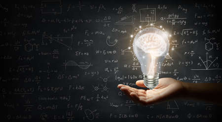 Hand holding a brain inside a light bulb on wall backboard or chalkboard background. Business bright...
