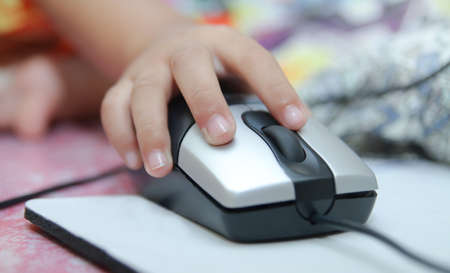 Child hand holds a computer mouse or keyboard. Child learns online and plays game on the computer at...