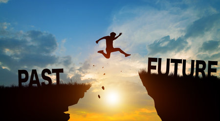Silhouette man jumping from PAST to FUTURE wording on cliffs with cloud sky and sunrise. Go ahead...