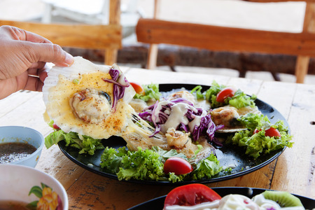 Baked Scallops with Cheese in black dish on wood table.