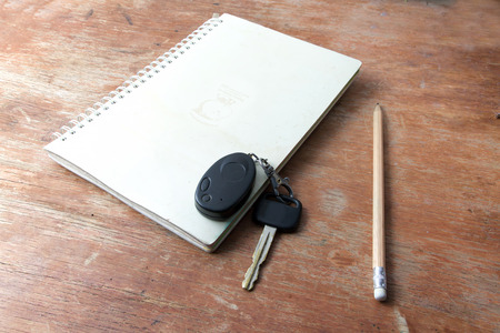 book note and pencil and key on the old wooden table. and remote alarm the car.の写真素材
