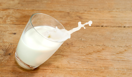 Glass of milk are falling move downward on a wooden tableの写真素材