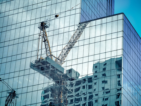 Construction tower cane reflected on the glass office building. Building development.