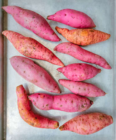 Raw Japanese sweet potatoes on an aluminum tray ready to be baked in the oven.の写真素材