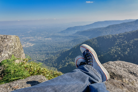 Leg of a man sitting on the edge of a cliff at the mountainsの写真素材