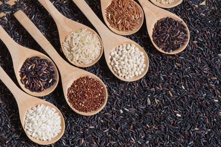 Top view different rice on wooden scoop with black riceberry background, Various rice organic on wooden spoon collectionの写真素材