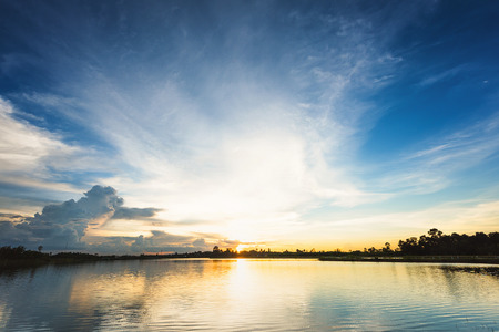 Sunset landscape with blue sky and fluffy clouds over lakeの写真素材