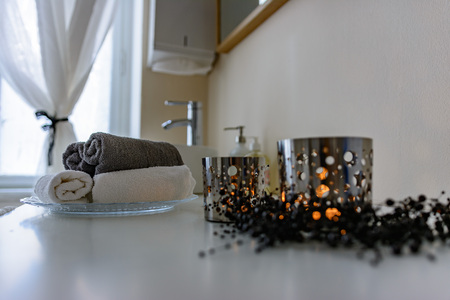 Bathroom still life of rolled towels and burning candles in cut out patterned metal candle holders on a vanity alongside the hand basin in a low angle view conceptual of personal hygieneの写真素材