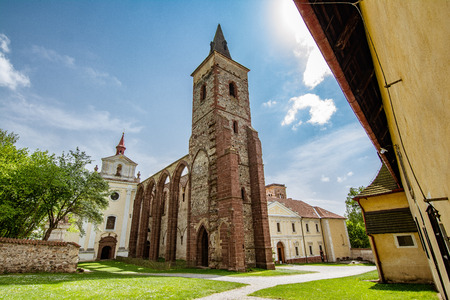 Old historic rural church with brick bell tower and arched Gothic entrance set in a quiet square with neat green lawns under a sunny skyの写真素材
