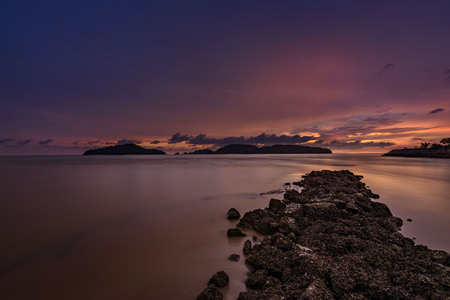 Colorful dark sunset with rocky coastline in foreground and small islands on the edgeの写真素材